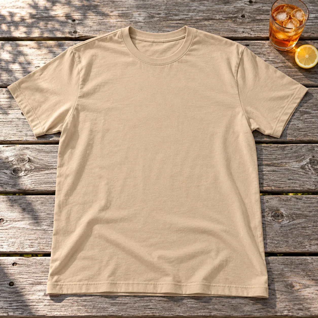 A soft sand cotton tee laid on a sunny picnic table beside iced tea