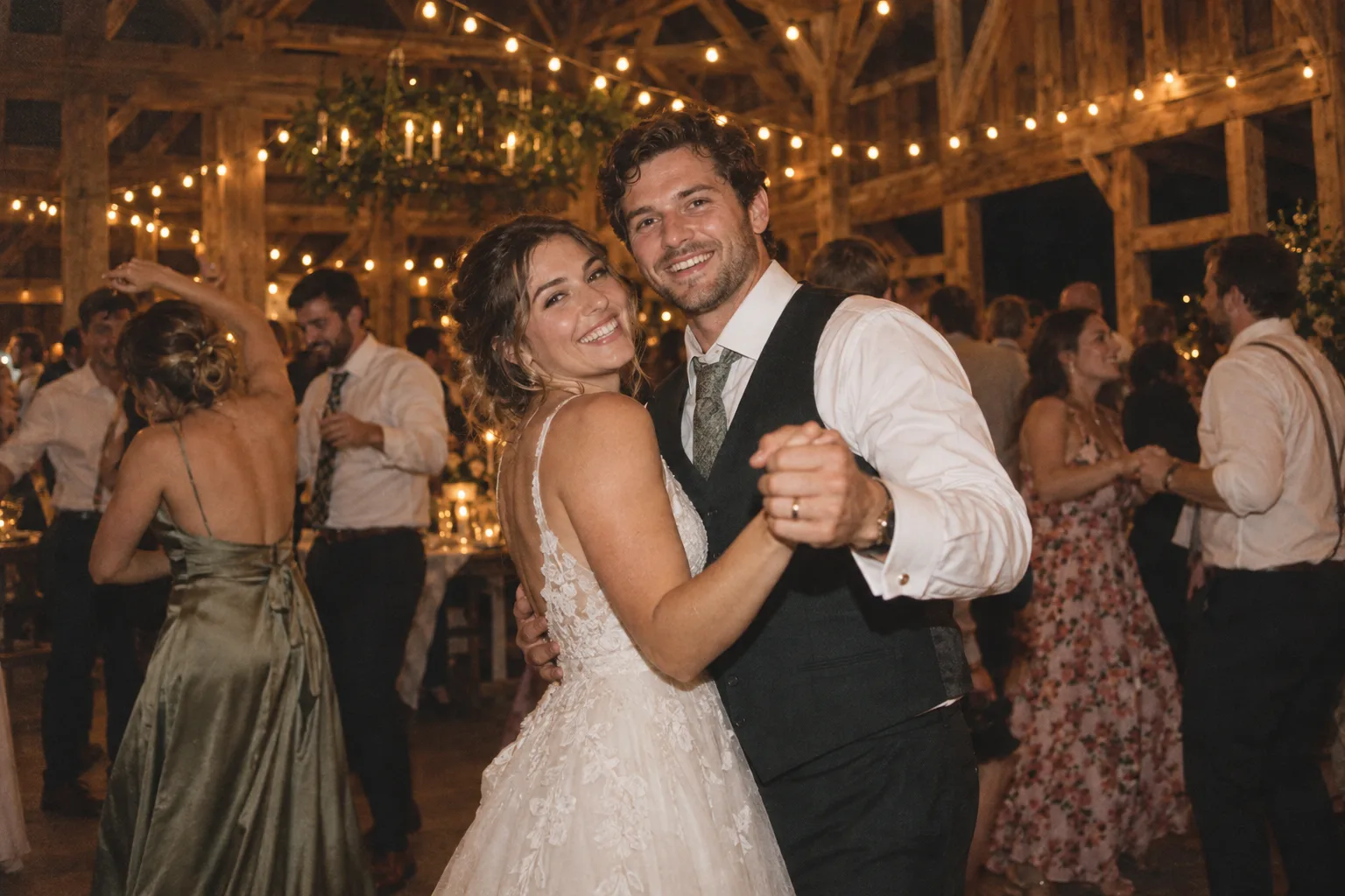 A couple dance together beneath the barn string lights.